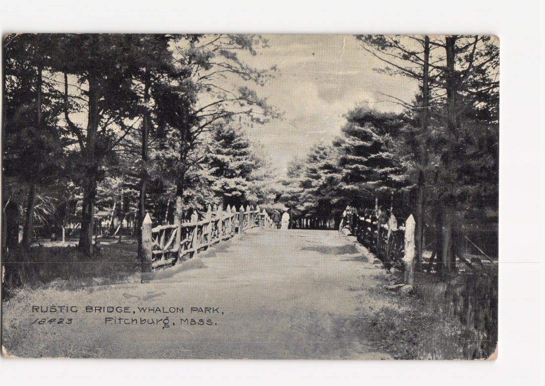 Vintage halftone postcard of Rustic Bridge, Whalom Park, Fitchburg, Massachusetts, postmarked 1909.: A rustic wooden bridge stretches through a wooded park. The bridge features railings constructed from natural logs and branches, guiding a path into the distance. Dense trees line both sides of the br