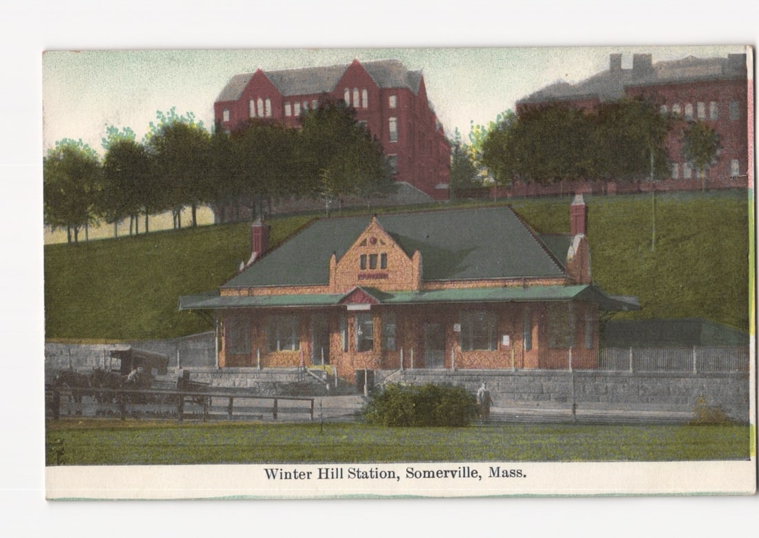 Winter Hill Station, Somerville, Massachusetts, Early 20th Century Train Station View Postcard: A detailed colored photographic print depicts Winter Hill Station in Somerville, Massachusetts. The station building, constructed of brick with a dark roof and a gabled central section, stands promine