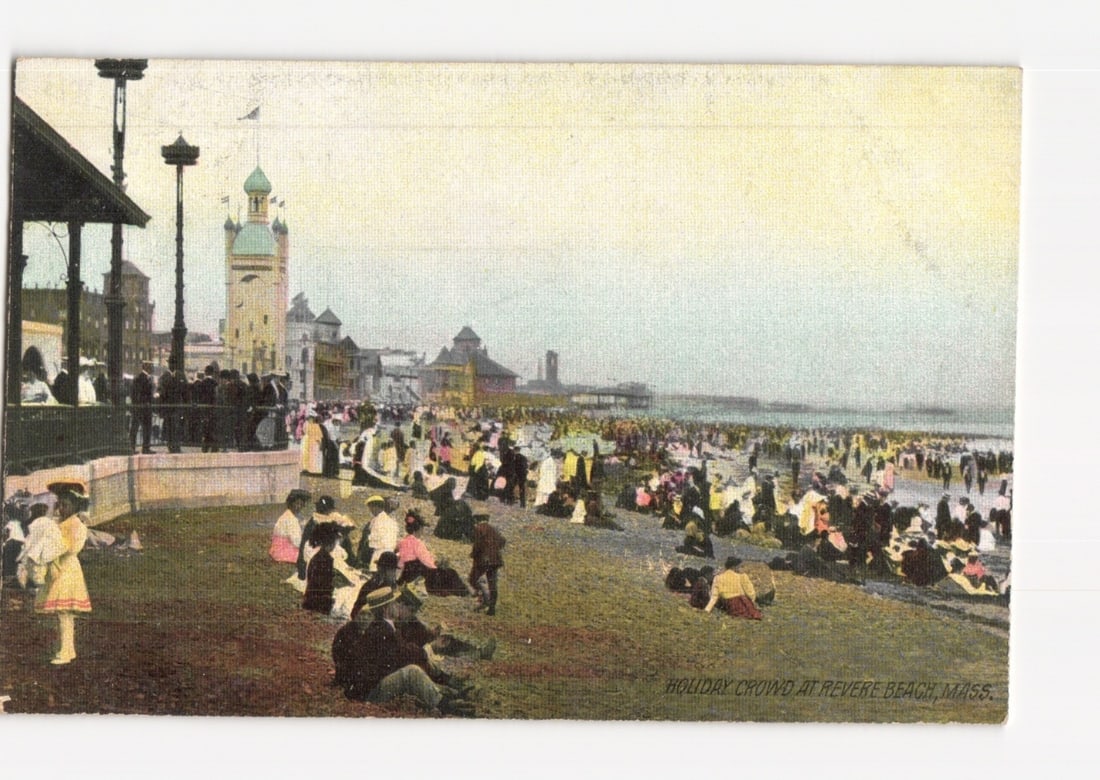 Holiday Crowd at Revere Beach, Massachusetts, early 1900s panoramic scene postcard.: A large crowd gathers on a grassy slope and sandy beach under an overcast sky. In the foreground to the left, a covered pavilion structure is visible, under which several individuals stand. People are