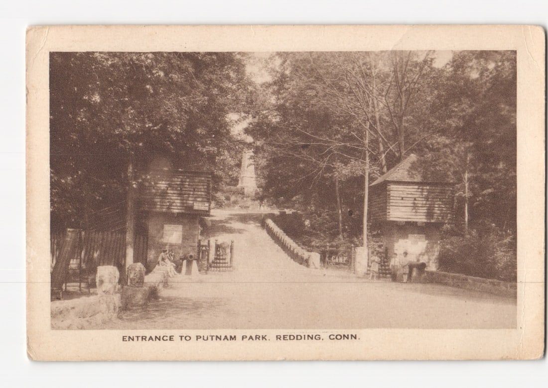 Sepia Real Photo postcard depicting the Entrance to Putnam Park, Redding, Connecticut, postmarked: A sepia-toned Real Photo Postcard illustrates the entrance to Putnam Park. An unpaved path ascends between two rustic wooden gatehouse structures, each with a steeply pitched roof, framed by dense tre