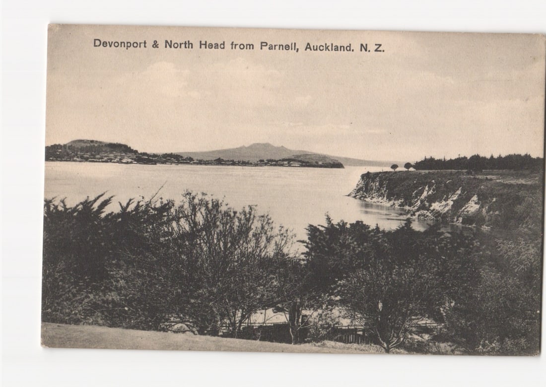 Panoramic view of Devonport & North Head from Parnell, Auckland, N. Z. vintage landscape postcard: A panoramic photographic print postcard depicting a wide landscape view across a body of water. The foreground features dense foliage, framing a bay with a prominent cliff face on the right. In the di