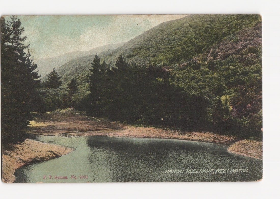 Scenic Chromolithograph Postcard: Kaikori Reservoir, Wellington, New Zealand, Early 20th C.: A chromolithograph postcard displays the Kaikori Reservoir in Wellington, New Zealand. The scene features a calm body of water in the foreground, reflecting the sky. Dense, dark green forest covers th
