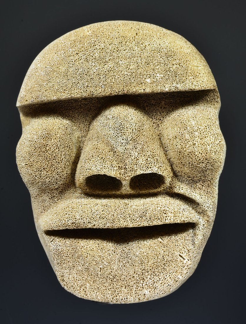 Arctic Peoples Inuit Carved Whale Bone Mask: North West Coast, 19th Century or older. Deeply carved rounded mask with grimacing facial expression, jutting chin, nice volumes. From a fossilized bone. Size: 8-3/8 inches H. Impressive and beautiful