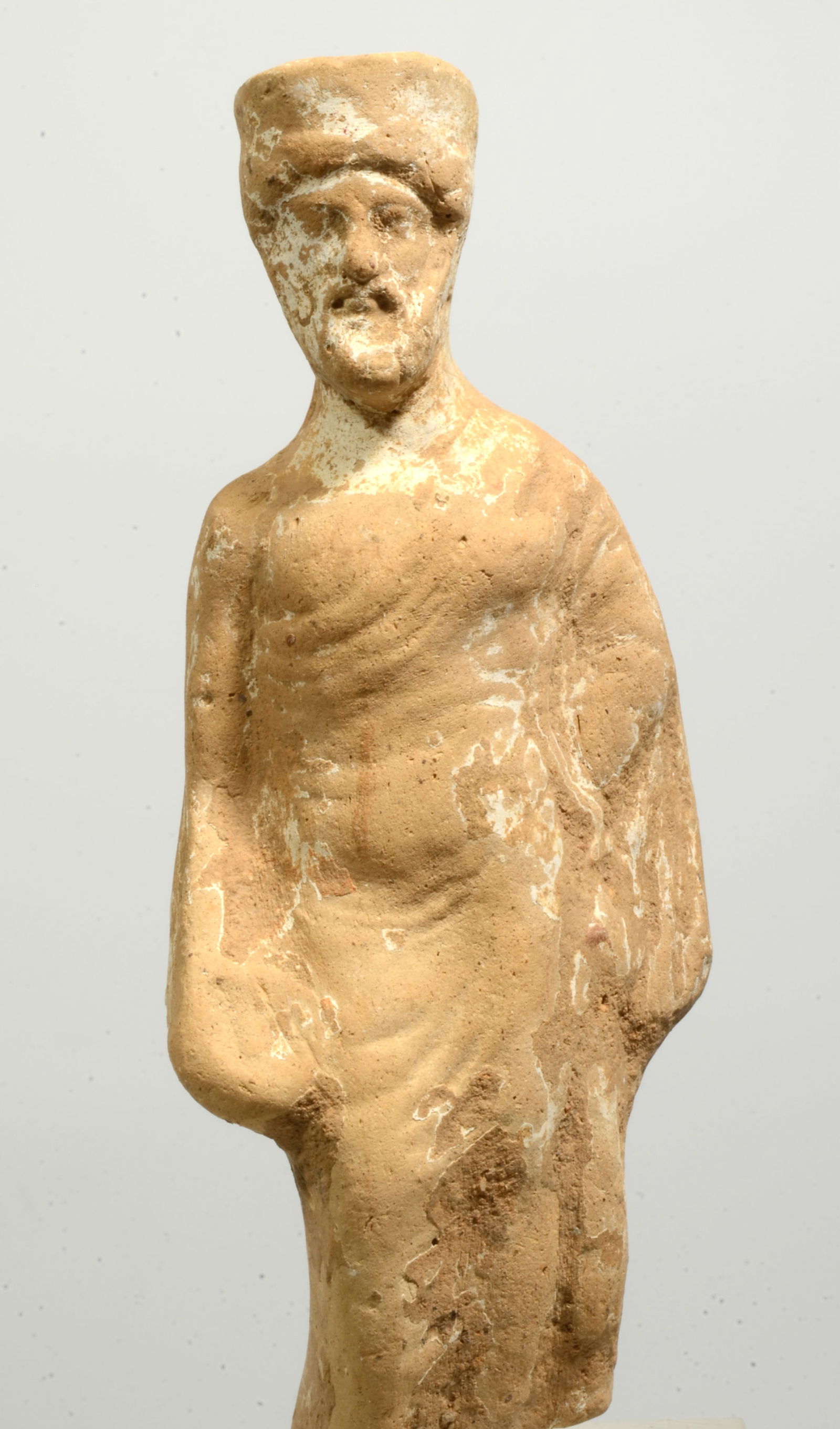 Greek Terracotta Standing Bearded Male: Circa 3rd to 2nd century BCE. Buff clay bearded votive figure wearing a flat cap and with long flowing drapery folds, he holds an offing phiale in his lowered right hand. Size: 5 inches (12.7cm) H.; 6