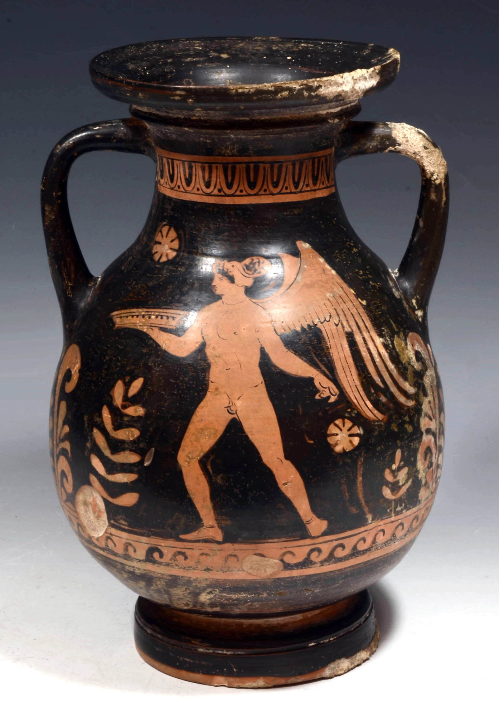 Apulian Red Figure Pottery Amphora: South Italy Ca 4th Century BC A strong vessel with lavish decoration, twin handles on shoulder and with a flared rim and long stem disc foot. A painted sepulchral scene is depicting a nude Eros, wings
