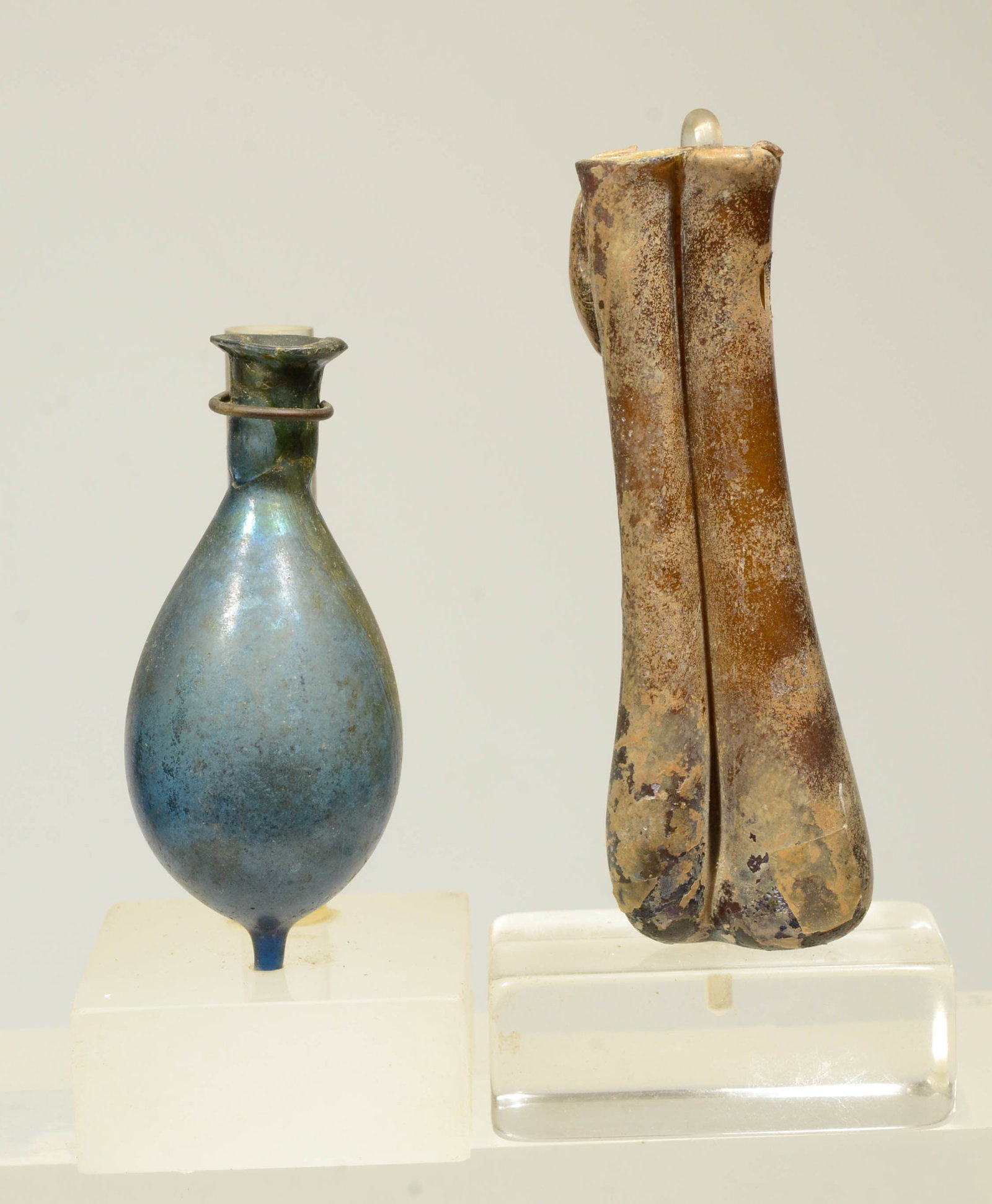 Roman Glass Double Unguent (Perfume Bottle) and Vial (2): Eastern Mediterranean circa 1st to 3rd Cent AD A yellow glass vessel made up of conjoined tubes with applied loop hanldes (one gone); along with a free blown blue glass vessel having a bulbous body an