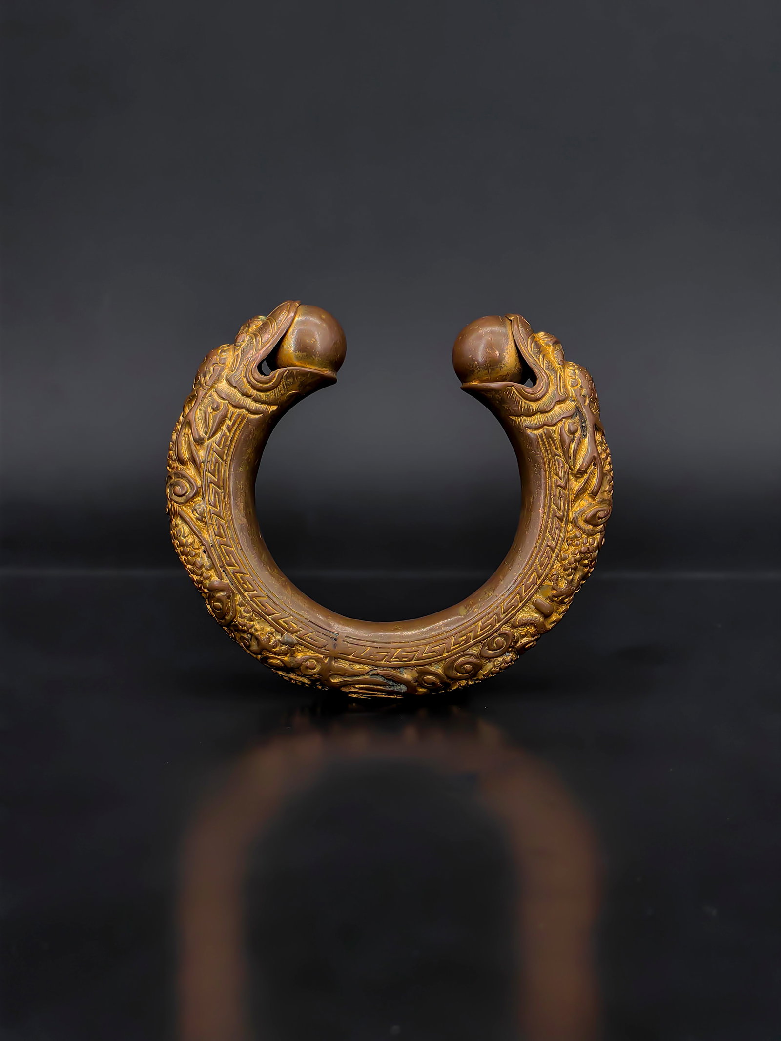 A Chinese Gilt-Bronze Dragon-Head Ritual Bangle: A 18th finely cast open-form gilt bronze bangle terminating in two confronting dragon heads, richly detailed with scales, flowing whiskers, and stylized cloud motifs. The exterior is further
