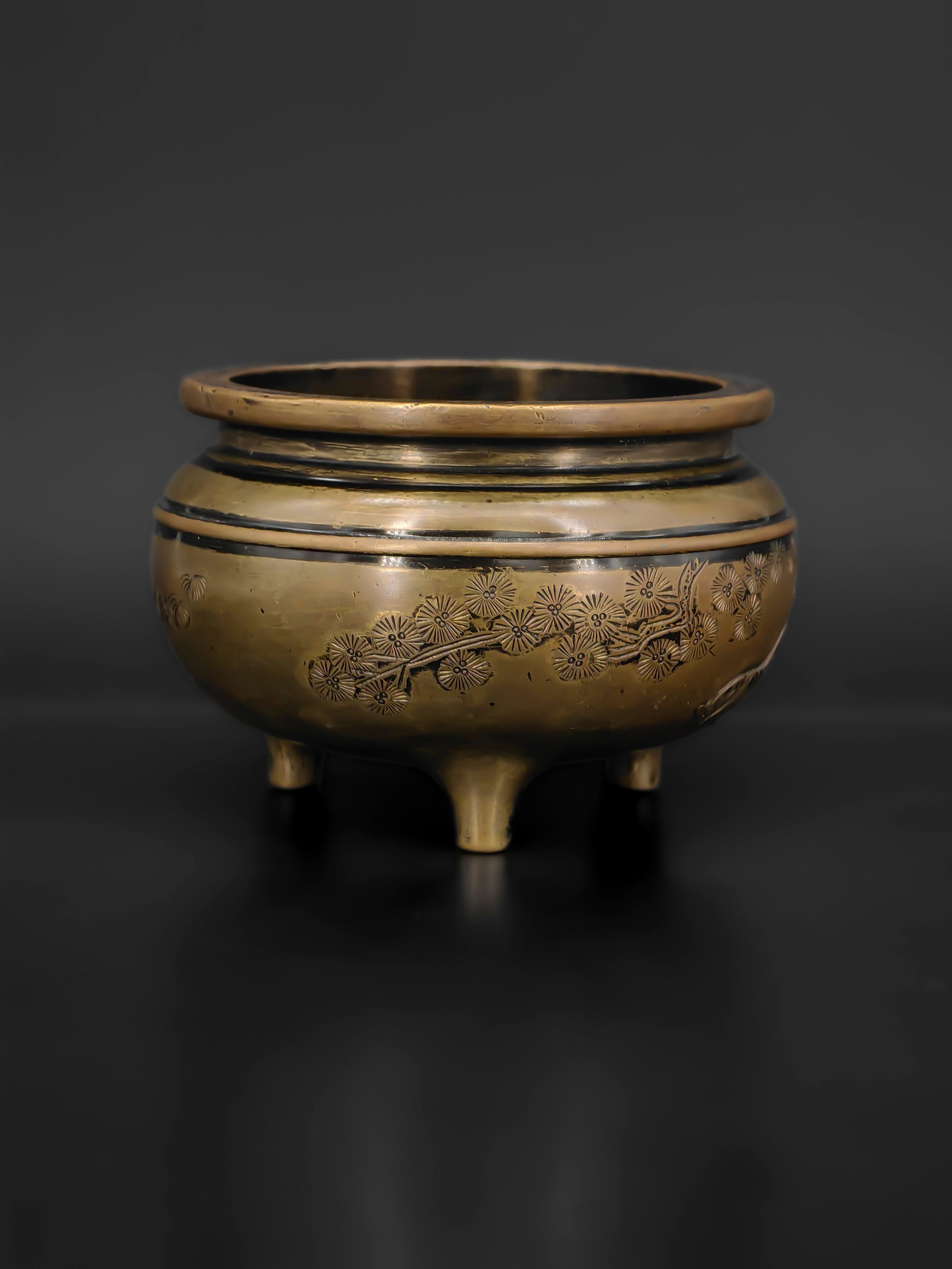 An Ancient Bronze Censer: A finely cast 18th bronze tripod censer of rounded form, raised on three short cabriole legs and surmounted by a broad, everted rim. The exterior is delicately engraved with blossoming branches and a