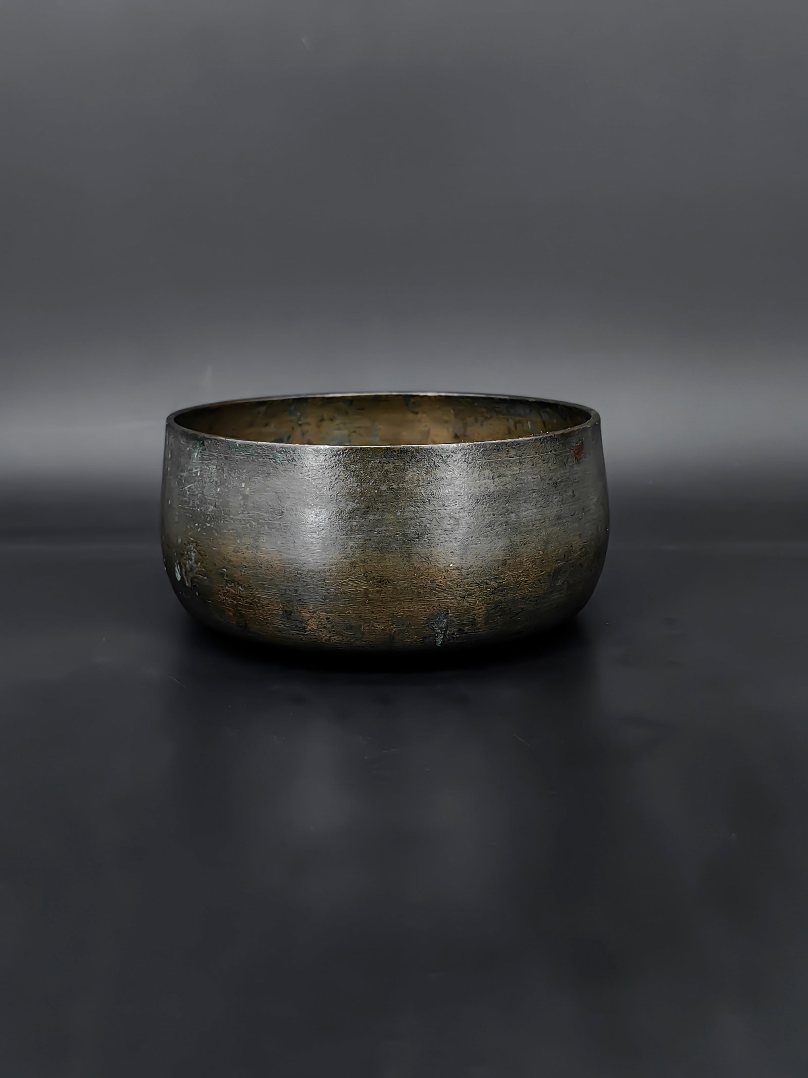 An Antique Bronze Bowl: This antique bowl is crafted from bronzeand features a simple, elegant form with a rounded body and slightly flared rim. The surface shows natural patina and oxidation from age, including small areas