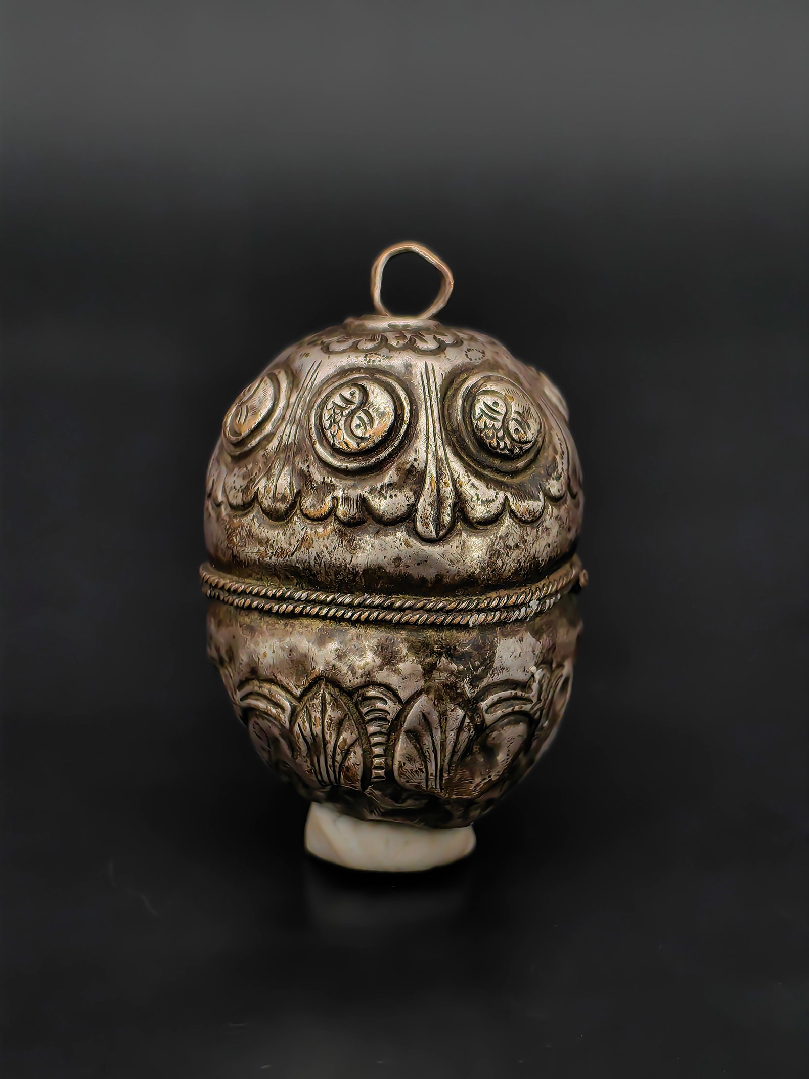 Antique Tibetan Nepalese Silver Repoussé Amulet Bead Pendant: This Antique Tibetan Nepalese Silver Repoussé Amulet Bead Pendant features a rounded, two-part form decorated with finely hand-worked repoussé patterns. The surface displays floral and circular