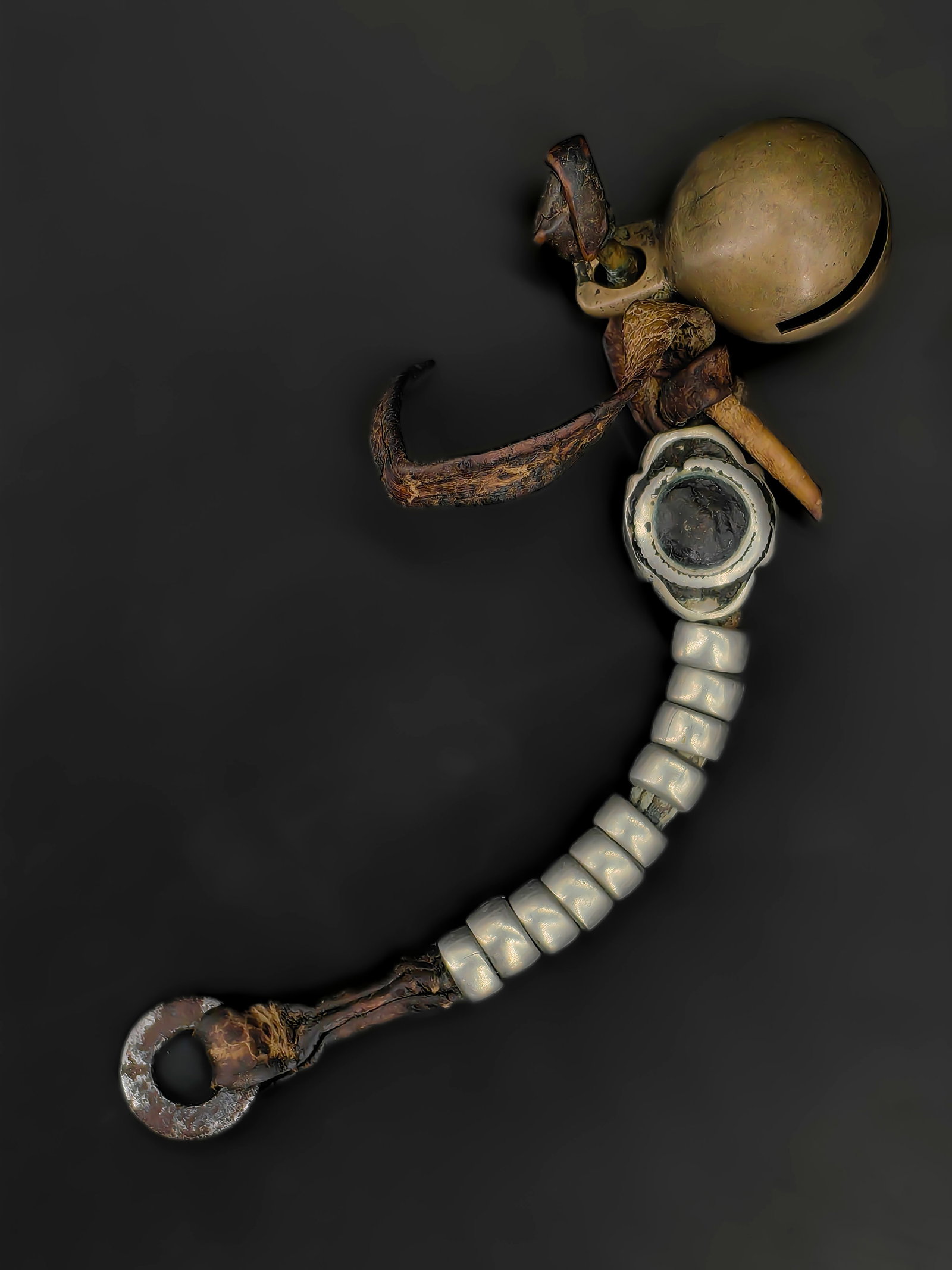 An Antique Tibetan Pendant Assembly: Antique Tibetan garment pendant, likely late 19th–early 20th century. The piece features a curved strand of pale beads threaded on cord, joined with leather bindings and a metal mount, suspending a