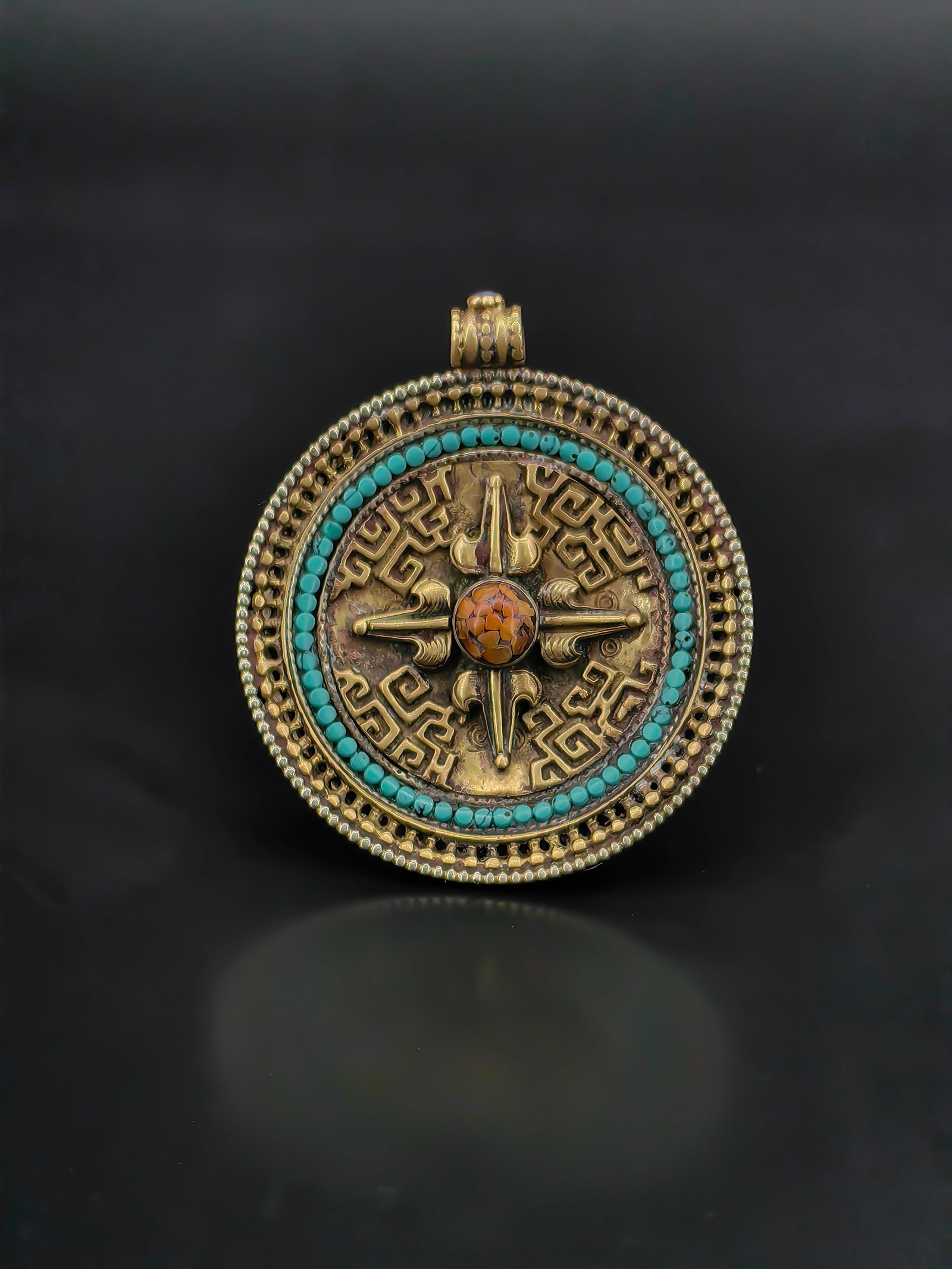 An Antique Tibetan Amulet: Antique Tibetan style pendant amulet featuring a circular metal body decorated with traditional auspicious motifs. The front displays a raised cross-shaped design surrounding a central cabochon