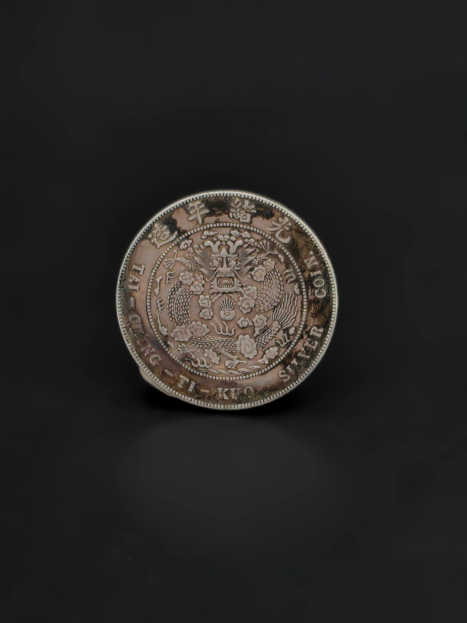 An Antique Chinese Silver Coin: Antique Chinese silver coin from the late Qing Dynasty, commonly known as a “Kiangnan Dragon Dollar.” The obverse features a finely detailed imperial dragon surrounded by clouds and the