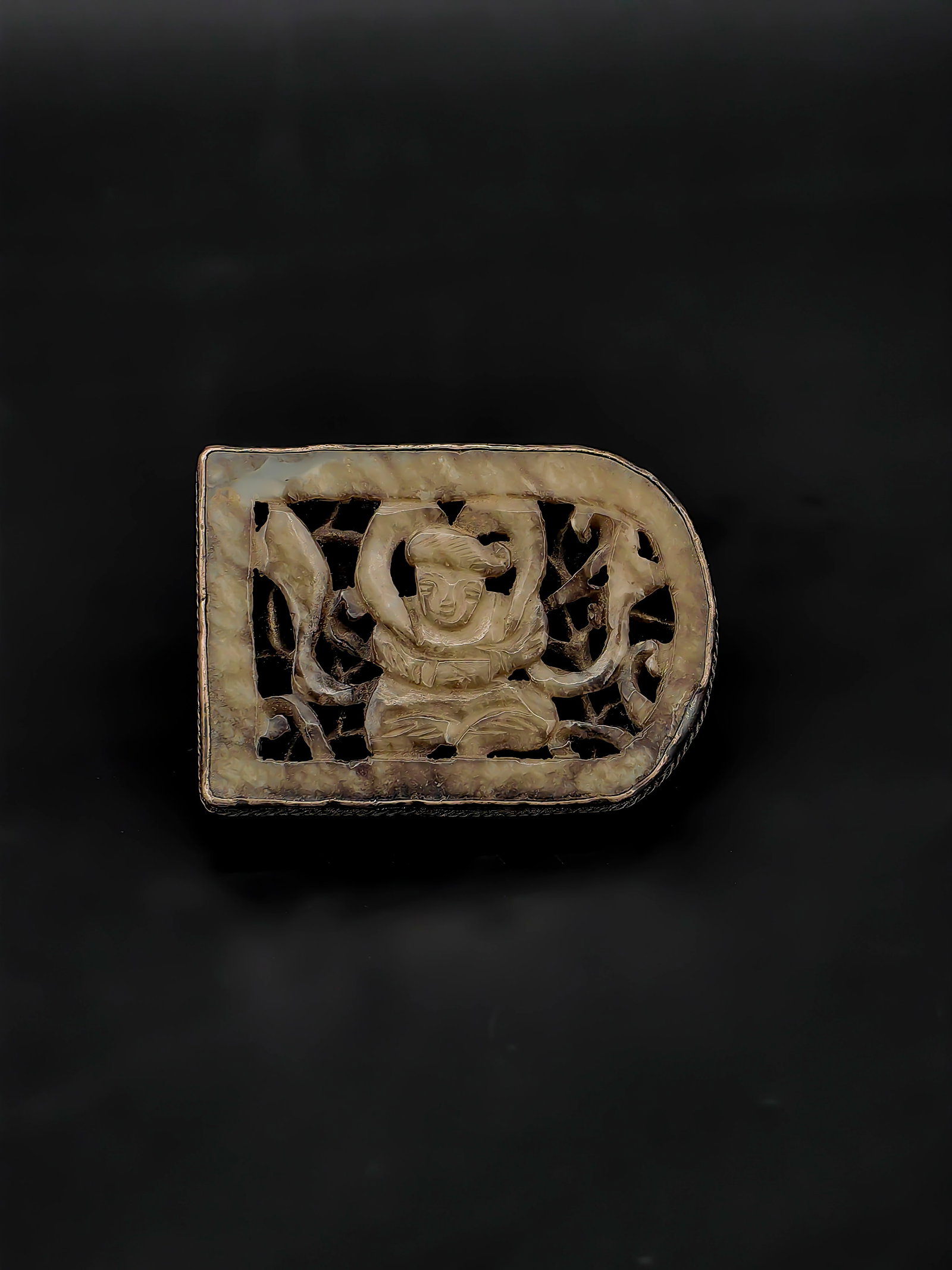 An Antique Chinese Jade Buckle: A Qing Dynasty silver-mounted jade buckle.This unique lot features an intricately carved openwork jade plaque depicting a traditional scholar figure. The jade displays a smooth texture with fluid, exp
