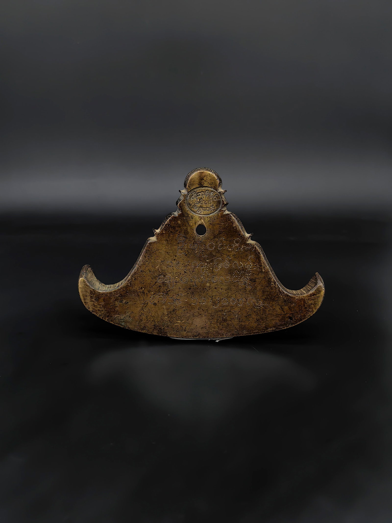 An Antique Burmese Inscribed Bronze Kyee-zee: This is a traditional Burmese triangular bronze gong, known as a Kyee-zee. It features a characteristic curved shape with upward-flaring wings and a suspension hole at the top. Both sides are