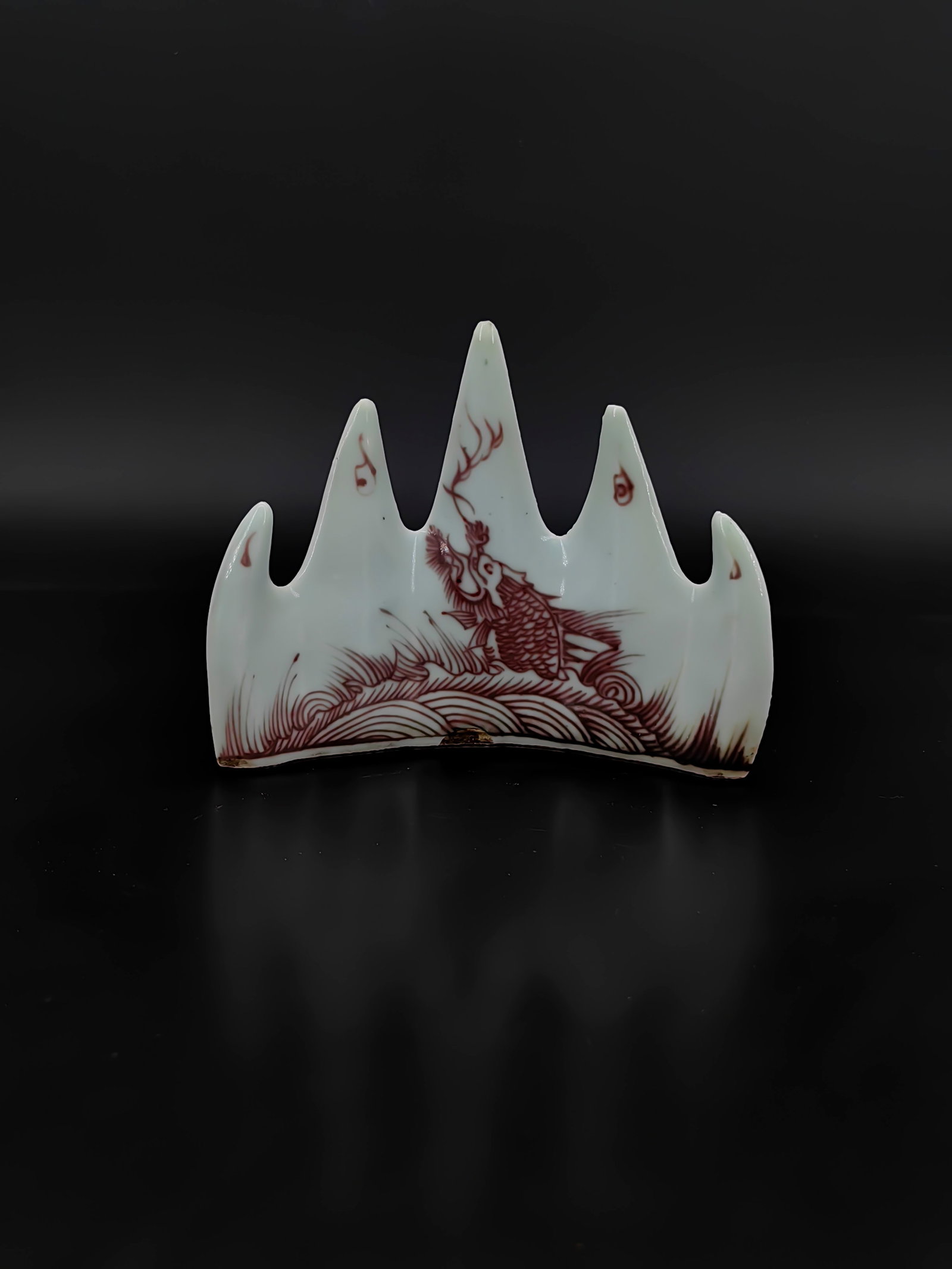 A Chinese Qing Dynasty Underglaze Red Mountain Brush Rest: This brush rest, approximately 10cm in height, is sculpted in the form of five mountain peaks, symbolizing the sacred mountains of China. It is covered in a smooth celadon-white glaze and decorated