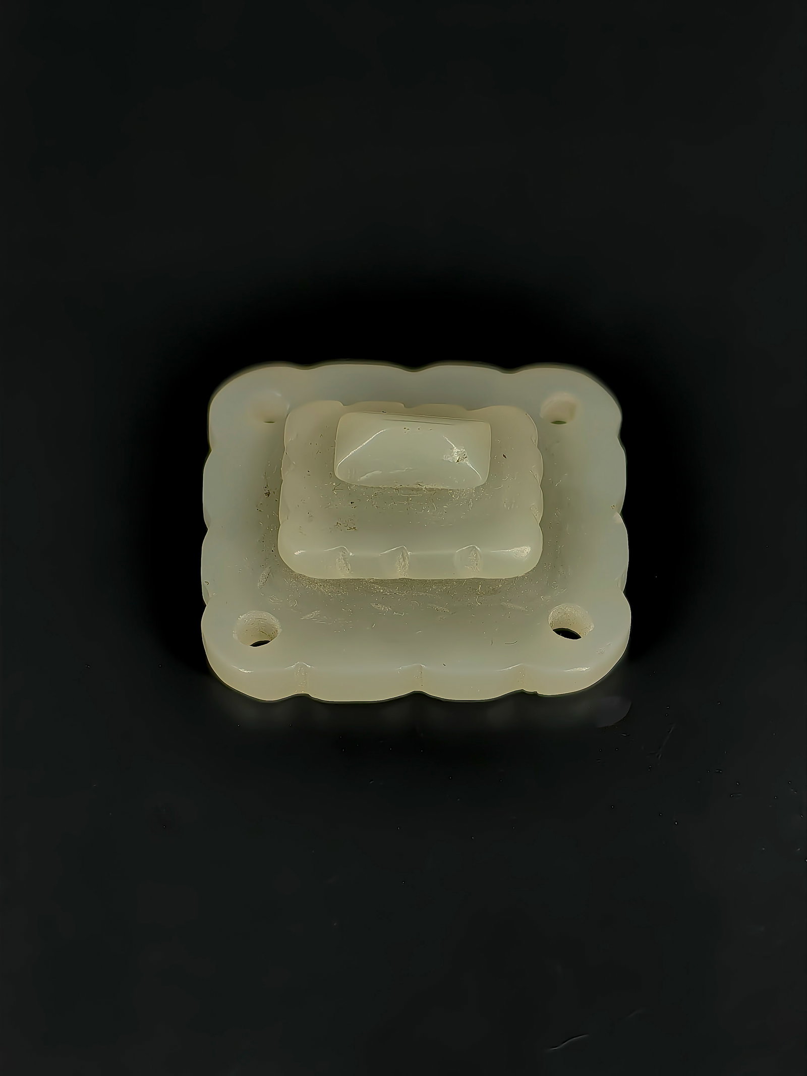 An Ancient Jade Ornament: This is an exquisite, multi-layered square jade inlay. The front features a three-tiered stepped design with scalloped edges. The base is equipped with four evenly distributed circular holes for
