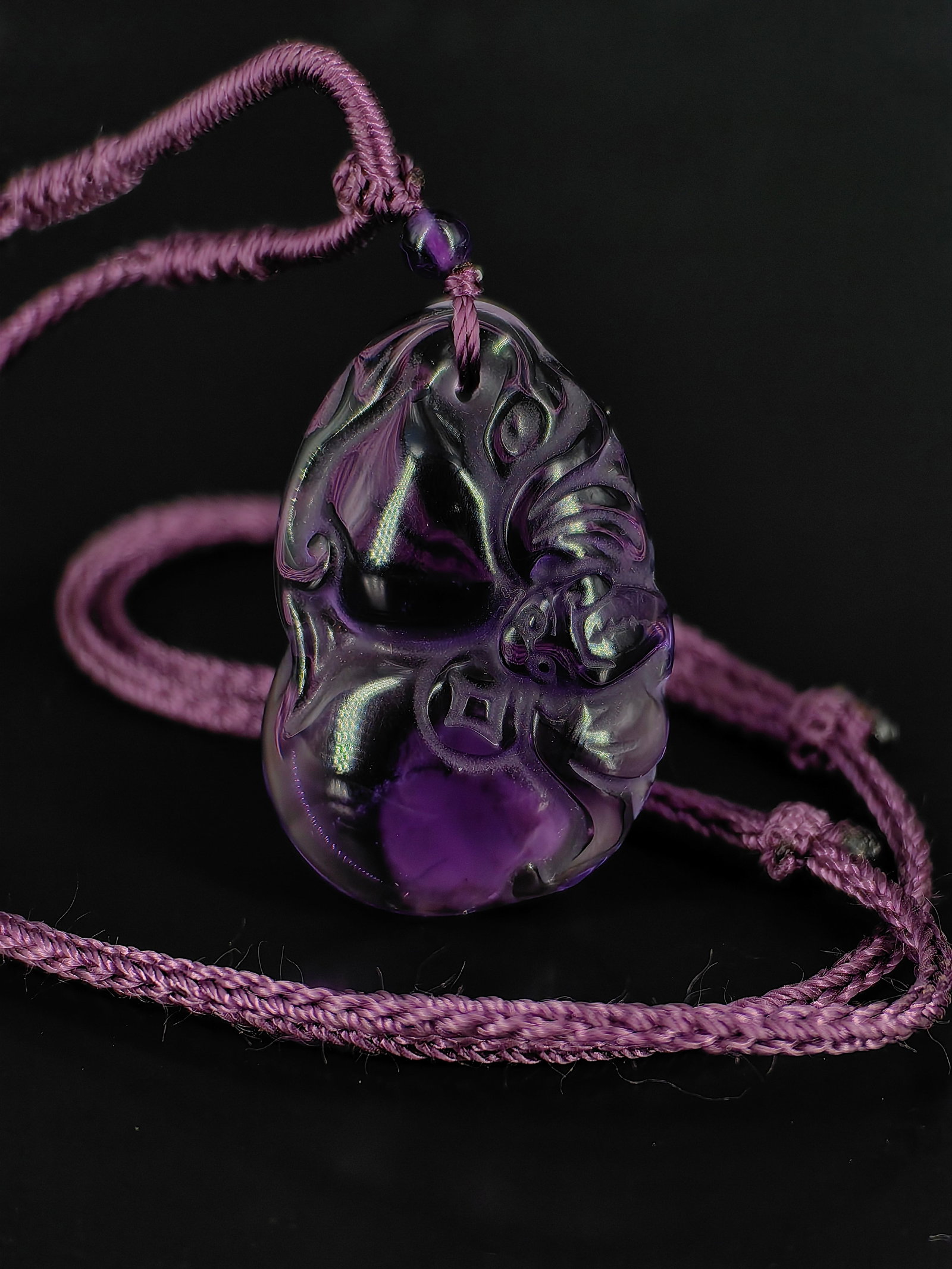 A Vintage Amethyst Carved Pendant: An exquisite amethyst carved pendant,completed with a matching purple braided cord and a small amethyst top bead.The front features a traditional auspicious design combining a plump longevity peach