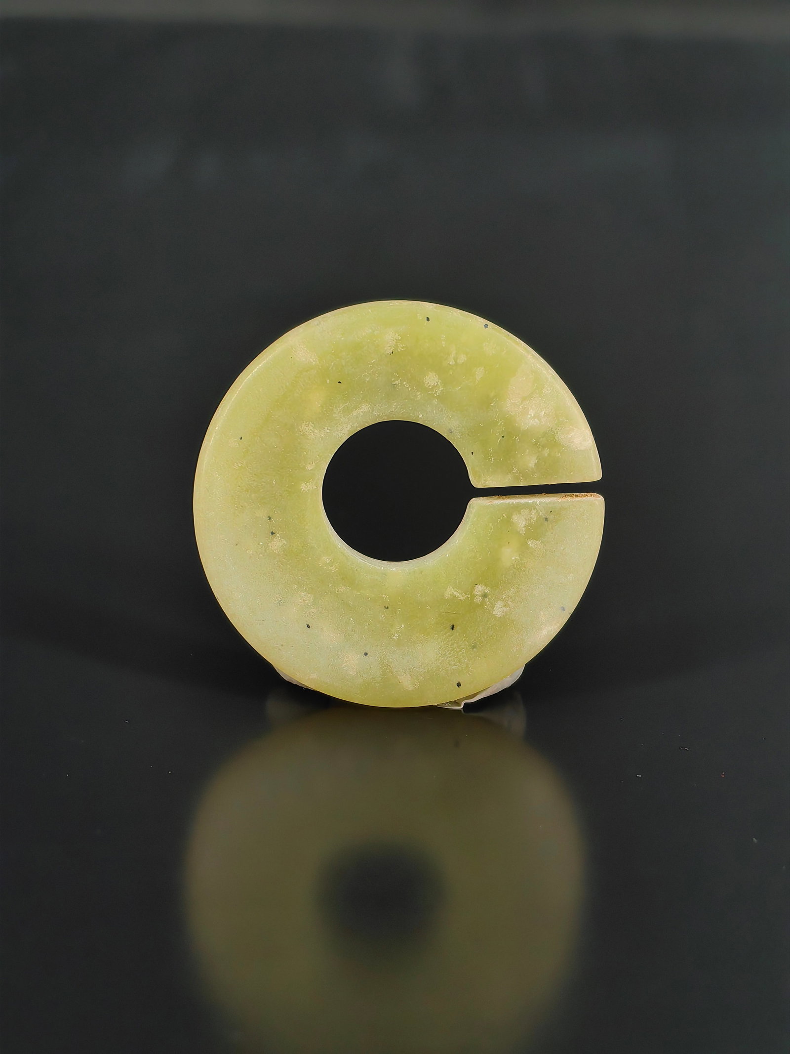 An Antique Jade Pendant: A yellow jade Jue (slit ring pendant) from the Republic of China period. The piece displays an elegant greenish-yellow hue, interspersed with natural white jade mottling and tiny black specks, all