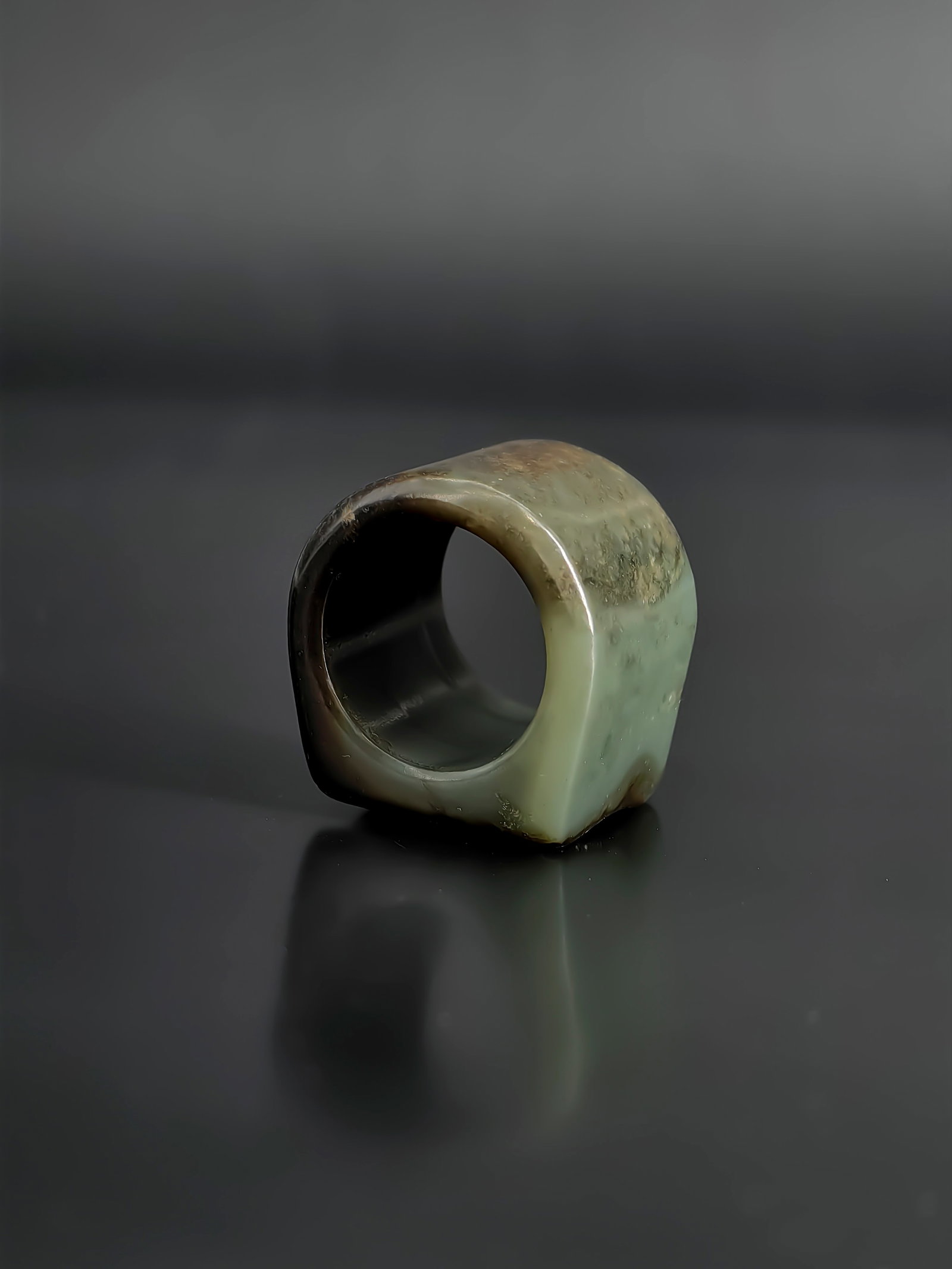 A Qing Dynasty Celadon Jade Archer's Ring: This collection features a Qing dynastyceladon jade archer's ring. Crafted from a finely textured celadon jade, the piece displays an elegant greenish tone heavily accented with natural dark brown