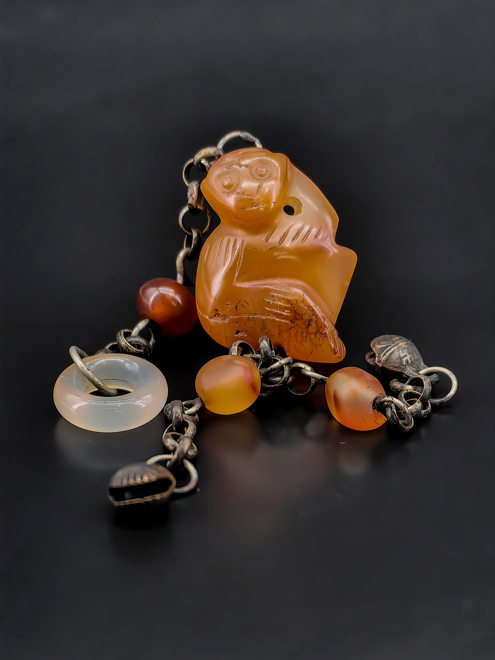 An Antique Agate Carving: This Qing Dynasty antique carved yellow agate monkey pendant is assembled with a vintage metal chain, an agate ring, and mini bells, measuring approximately 22 cm in total length with a charming,