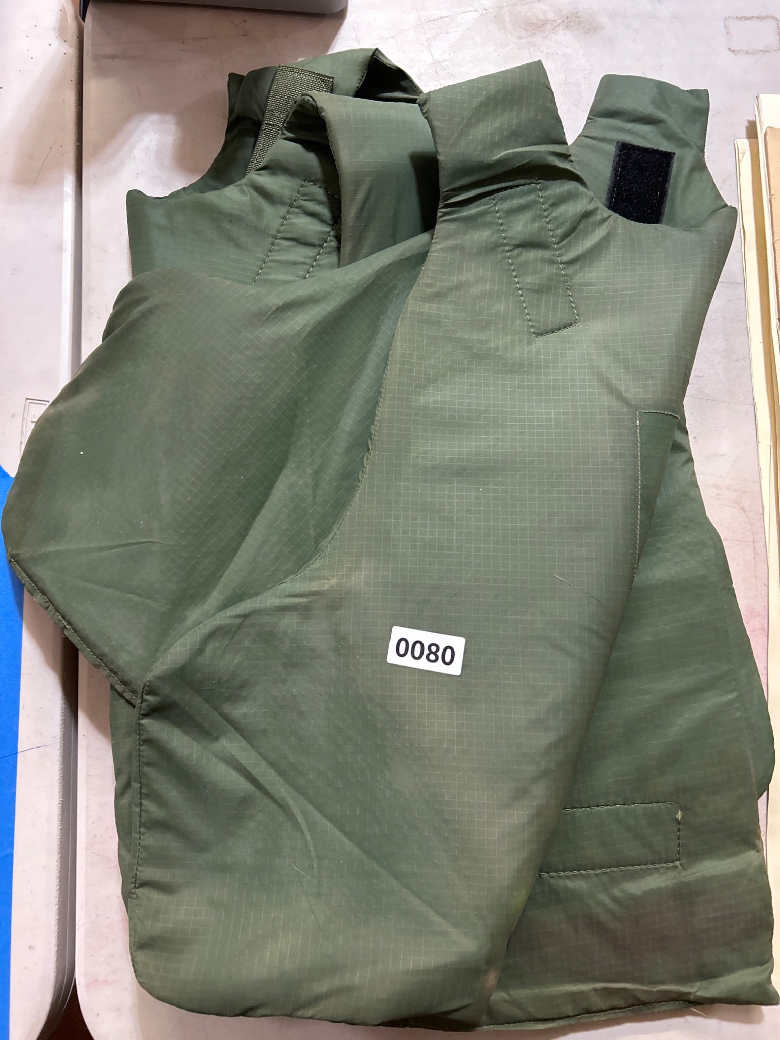 Green Ballistic Protective Vest: Green ballistic protective vest with Velcro closures, designed for personal body protection. Size and manufacturer not specified. Sold as is where is.The only lots that we in-house pack and ship are f