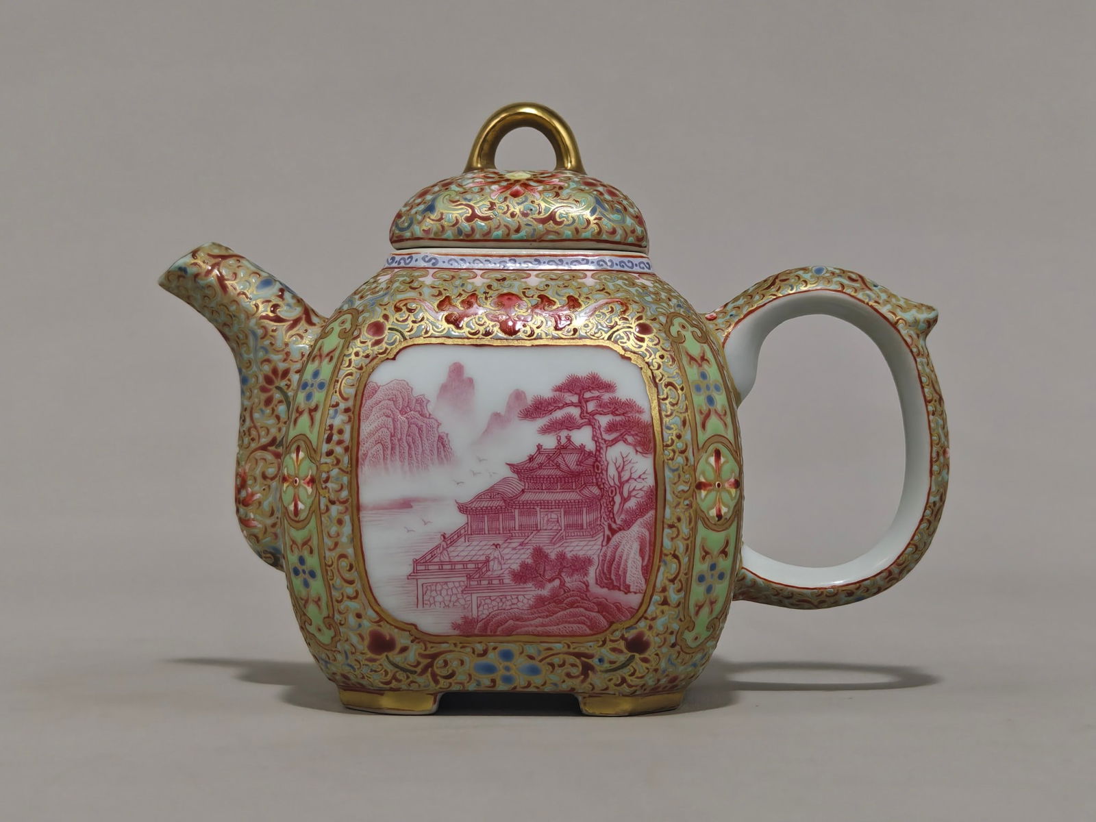 A teapot with enamel and gold decoration of a landscape pattern with a window, bearing the mark of: It is 11 cm high and 15 cm in diameter.