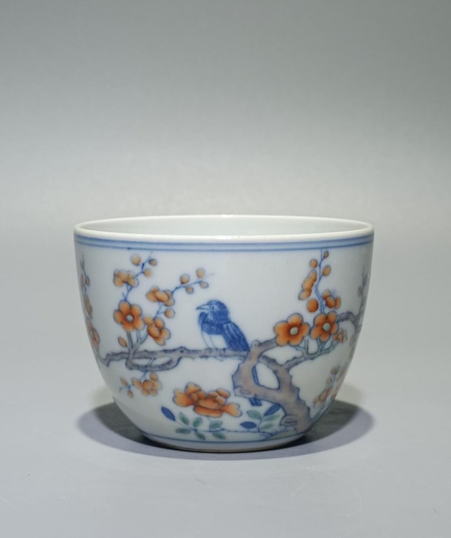Chinese Qing Kangxi Mark, Doucai Magpie Climbing Plum porcelain Cup: This is a beautiful porcelain cup decorated with a traditional-style painting. The design features a blue bird perched on a tree branch with orange flowers and green leaves, rendered in a delicate and