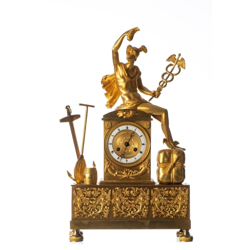 French 19th century "Mercury" clock in gilded bronze: A "Mercury" clock resting on a rectangular base decorated with cornucopias and flowers. It features a white enamel dial with Roman numerals and a chased bronze plate. The movement is housed within a r