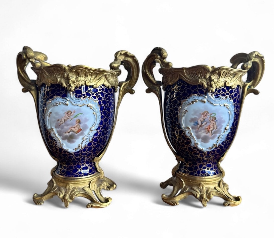 Meissen - Pair of vases with cupids: Pair of porcelain vases made by the Meissen factory. The body is covered with a cobalt blue glaze and gilt circles. The front features a medallion with two cupids in clouds, and on the other side, flo