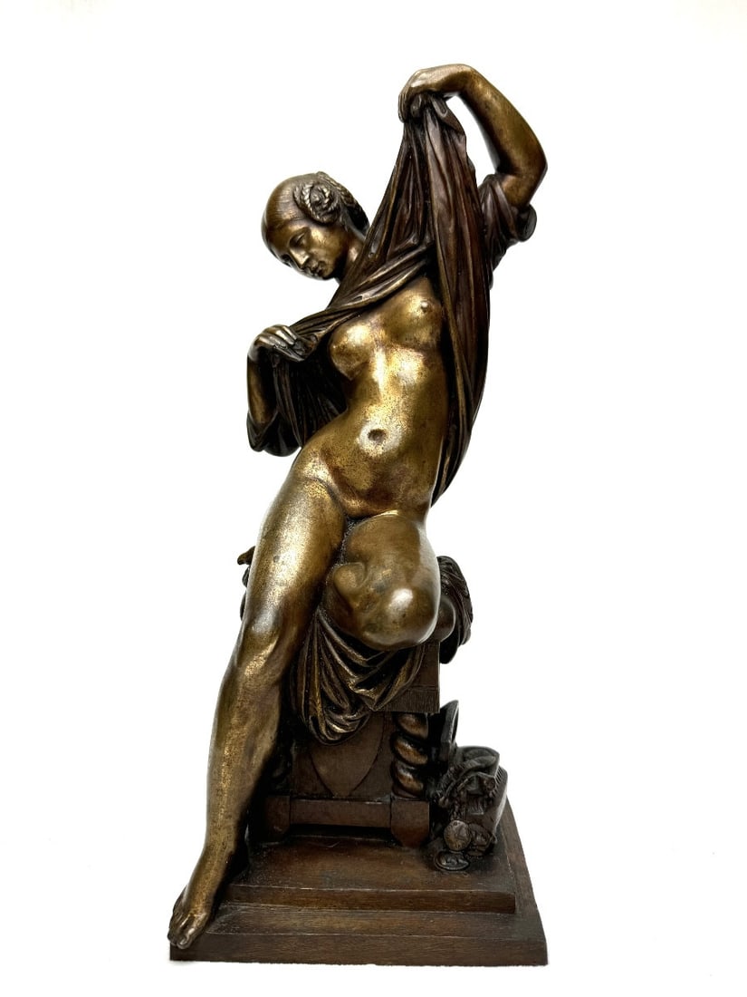 Bronze Sculpture of a Seated Woman Undressing: A bronze sculpture with a golden-brown patina, in the style of James Pradier, depicting a woman with braided hair, seated on a stool and undressing. On the floor beside the stool is a chest containing