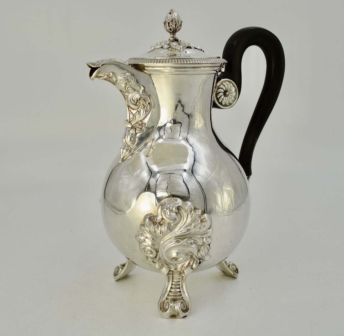 Silver ewer, France, 19th century circa 1886: A silver coffee pot with a pear-shaped body, resting on three scrolled feet with foliate attachments. The "duck" spout is decorated in relief with scrolling foliage. It has a curved handle of blackene