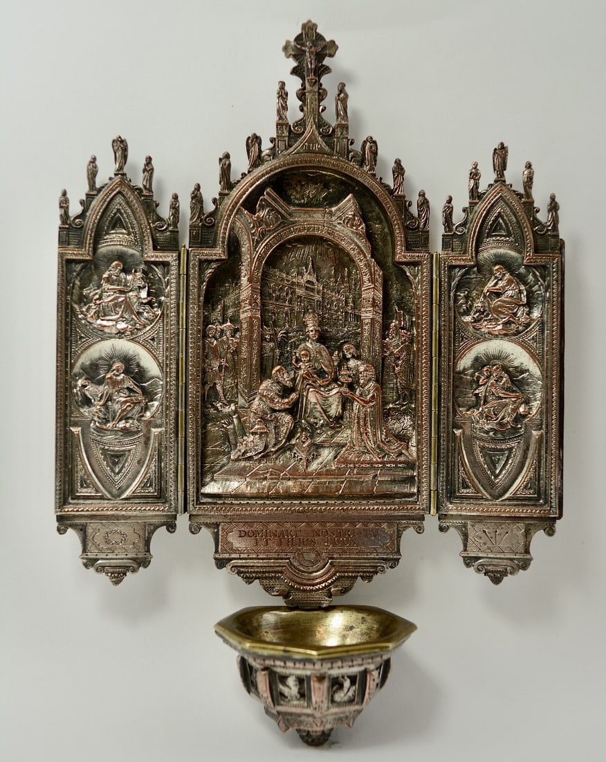 Wall-mounted holy water font, triptych, France 19th century.: A wall-mounted copper holy water font, formerly silvered, executed in the form of a Gothic triptych.The central panel depicts the Adoration of the Magi.The two hinged side panels feature the four Evan