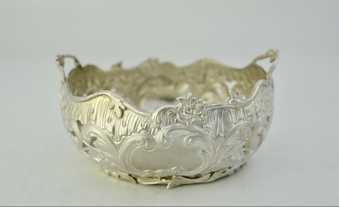 Silver Basket, Hanau, Circa 1900, Germany: A silver basket, repoussé, chased, and pierced, with a flat base and oval shape with a scalloped rim.The slightly domed body is decorated in the Rococo style. Two blind medallions surrounded by acant