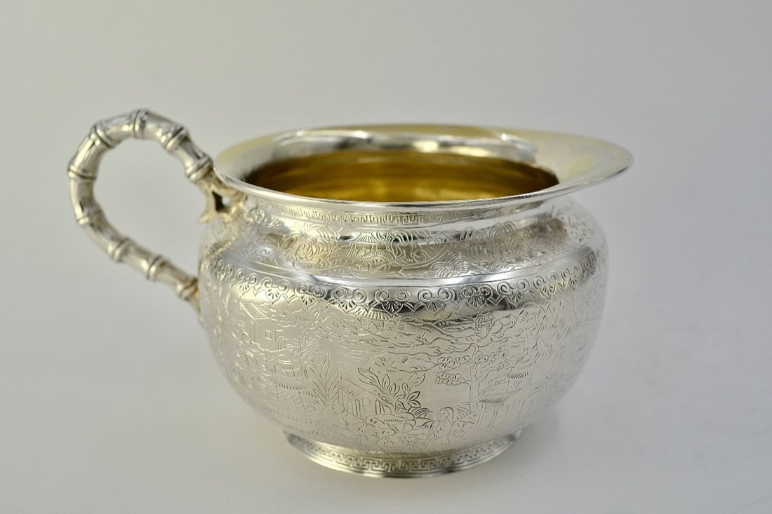 Silver Milk Jug, by Duponchel, Goldsmith, Circa 1850: A silver milk jug resting on a circular foot, with a bulbous body and a narrow rim forming a flared lip and a spout. The body is entirely engraved with chinoiserie motifs depicting a jumble of village