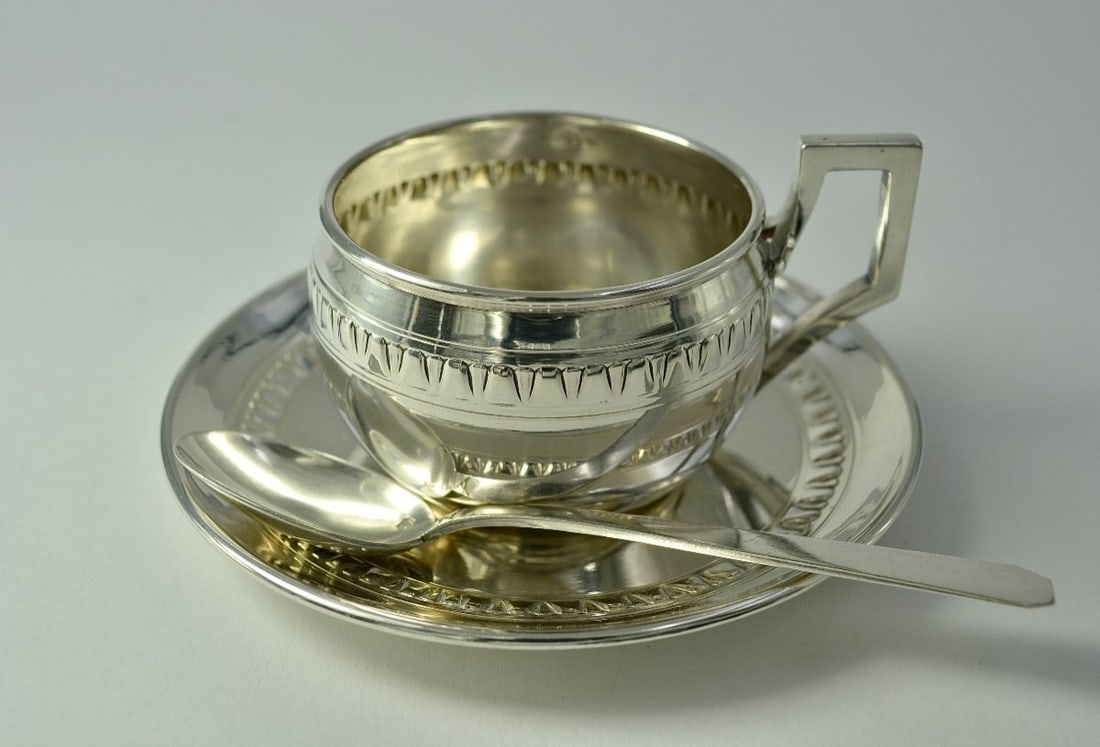 Art Deco. Silver Cup and Saucer, France, Early 20th Century: A cup resting on a base and its matching saucer in repoussé silver, with a bulbous body decorated with a geometric motif. The high handle is made of cast silver and is rectangular in shape. Art Deco