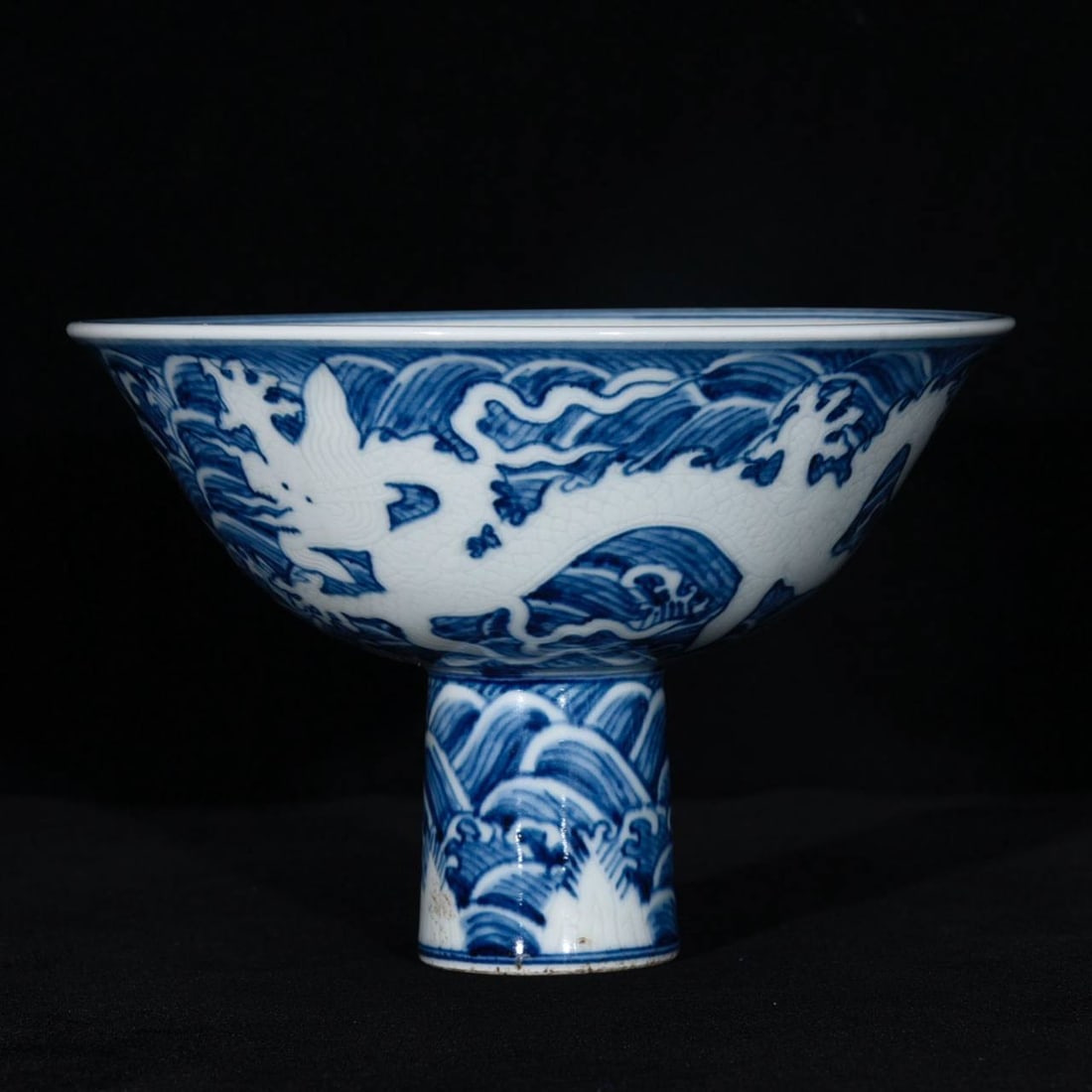 Ming Dynasty Xuande period blue and white carved high-footed bowl with a design: Ming Dynasty Xuande period blue and white carved high-footed bowls with a design of dragons amidst waves.Height: 11.5cm; Diameter: 16.8cm