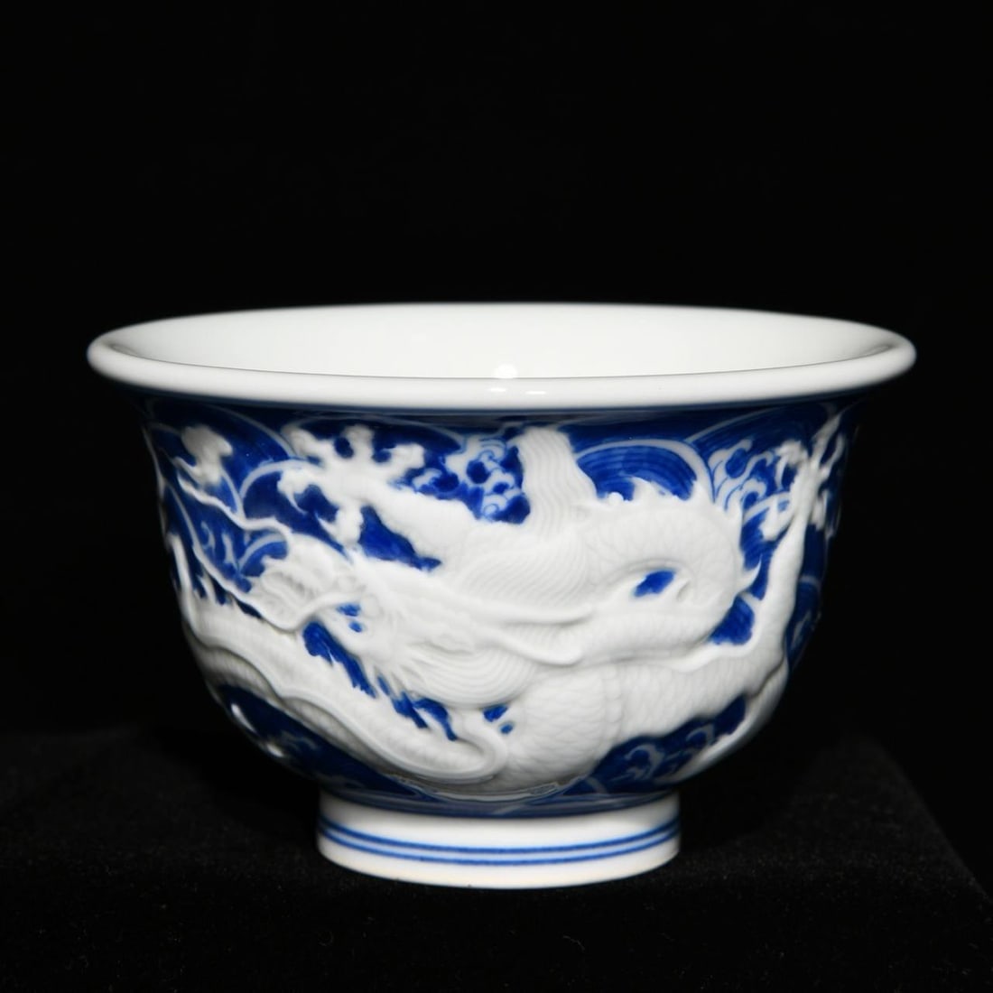 A Qing Dynasty Qianlong period blue and white porcelain cup with relief design: A Qing Dynasty Qianlong period blue and white porcelain cup with relief design of a dragon amidst waves, 6cm high and 9.5cm in diameter.