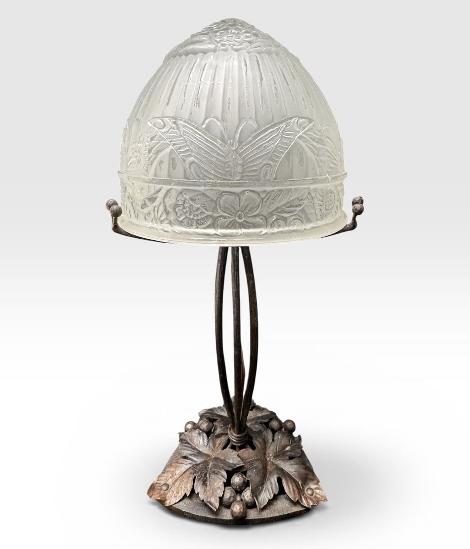ART DECO WROUGHT IRON LAMP DECORATED WITH FLOWERS AND BUTTERFLIES.: Art Deco mushroom lamp in pressed, molded, satin-finish glass decorated with stylized flowers and butterflies in relief. Wrought iron mount with three clamps on a hammered base decorated with foliage