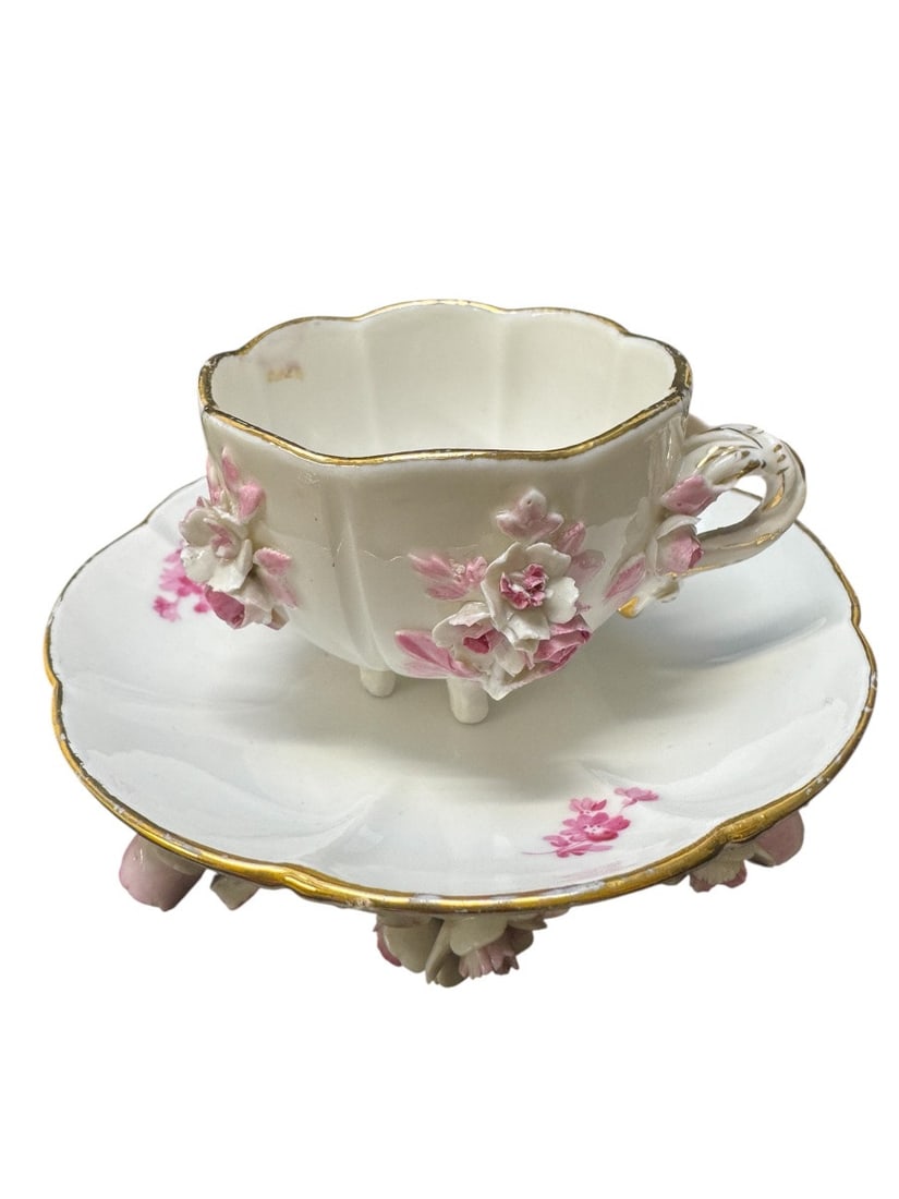 MEISSEN - CUP AND SAUCER DECORATED WITH FLOWERS AND ROSES.: Meissen porcelain cup and saucer with polychrome decoration and gilt details, applied porcelain flowers and leaves, and painted flowers. The cup and saucer rest on six small feet. Blue crossed swords