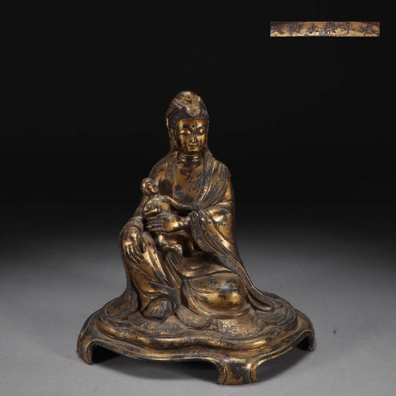A Ming Dynasty Finely Cast Bronze Gilded Guanyin Seated Statue with a Child: Size :Height 25.2cm, Width 23cm, Weight 3.9kgMade in the Yongle period of the Great Ming DynastyGuanyin wears a hood, with delicate features, kind eyes, and a serene and dignified expression. She wear