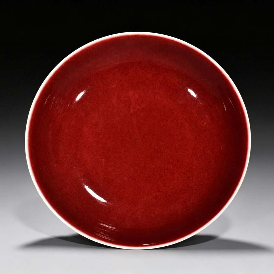 A round dish with a red glaze from the Qianlong period of the Qing dynasty: A round dish with a red glaze from the Qianlong period of the Qing dynasty (with an inscription by Emperor Qianlong). Height: 4.6 cm; Width: 22.6 cm.