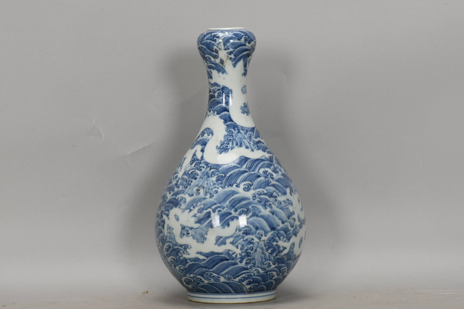 A blue-and-white garlic-head vase with a dragon design amidst waves: A blue-and-white garlic-head vase with a dragon design amidst waves, dating from the Chenghua period of the Ming Dynasty. Height: 32.3cm, Mouth diameter: 4.2cm, Belly diameter: 17.6cm, Base diameter: 