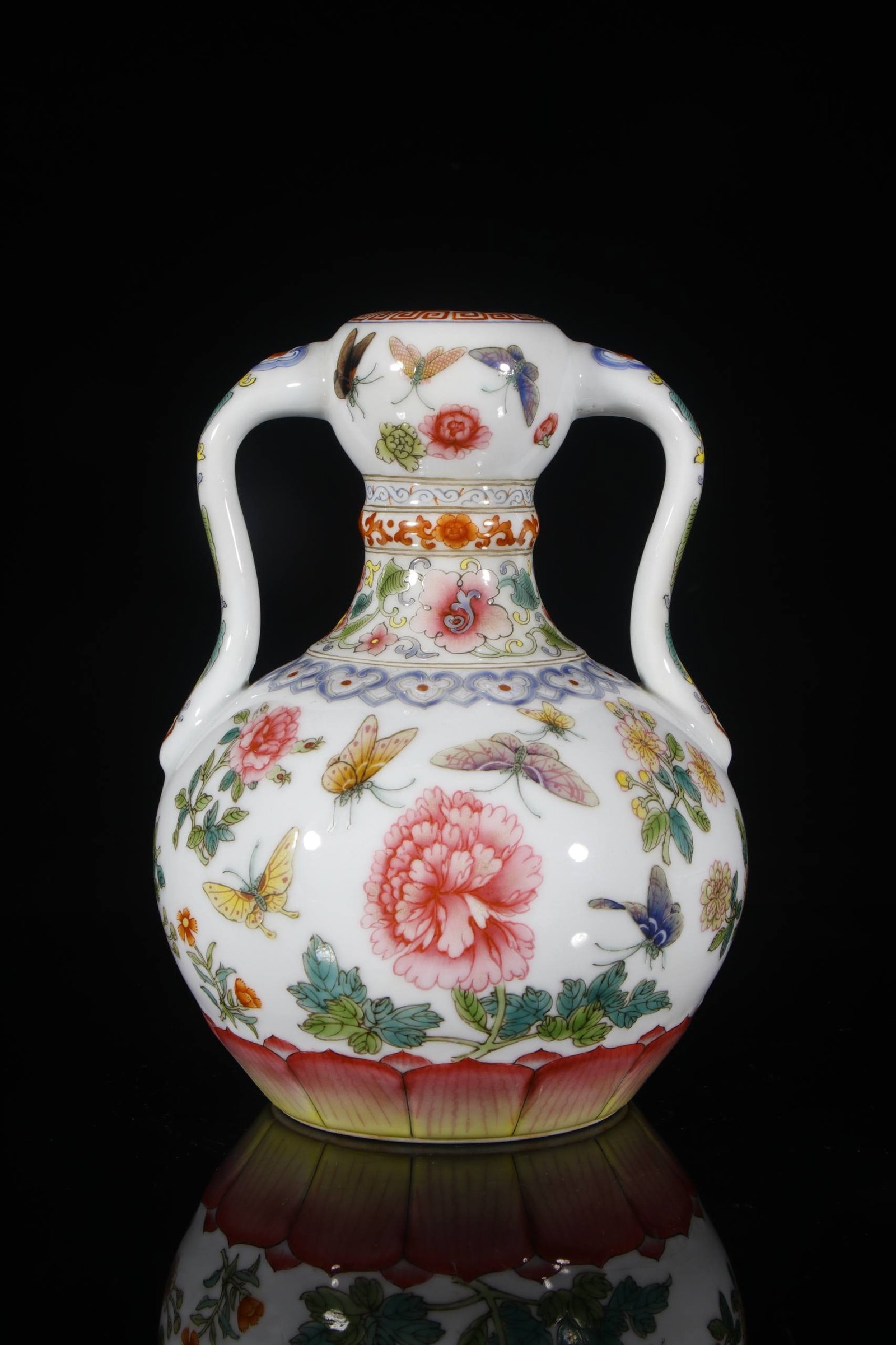 A Qing Dynasty Qianlong period famille rose enamel vase: A Qing Dynasty Qianlong period famille rose enamel vase with double handles and a design featuring a hundred butterflies and peonies. Height: 23.5 cm, Mouth diameter: 4 cm, Base diameter: 10 cm.
