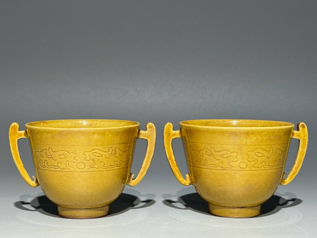 A Qing Dynasty Kangxi period (1666-1665) double-eared cup: A Qing Dynasty Kangxi period (1666-1665) double-eared cup with a delicate yellow glaze and incised kui-phoenix design. Height: 4.9cm Width: 7.8cm