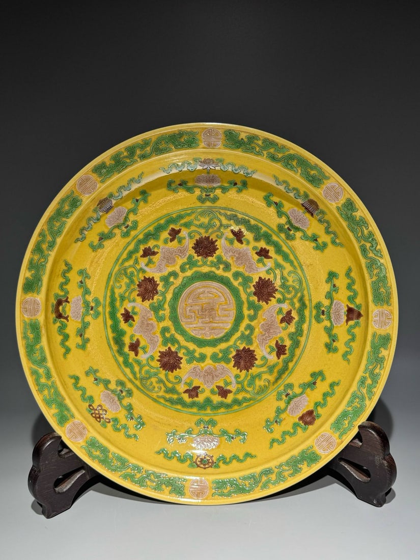 Made during the Yongzheng reign of the Qing Dynasty, a plain sancai (three-color glazed) dish: Made during the Yongzheng reign of the Qing Dynasty, a plain sancai (three-color glazed) dish with an outer lotus base supporting eight auspicious symbols, five blessings, and longevity symbols. Diame