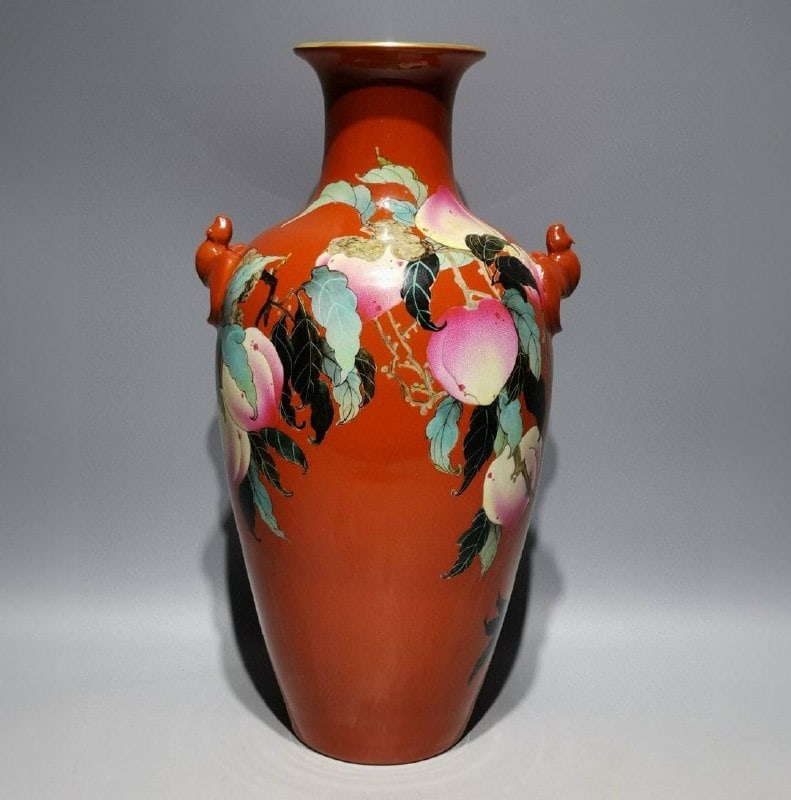 A coral-red enamel vase with nine peaches and bat-shaped handles: A coral-red enamel vase with nine peaches and bat-shaped handles, decorated with gold enamel and made during the Qianlong reign of the Qing Dynasty. Height: 34.2cm, Width: 18.5cm