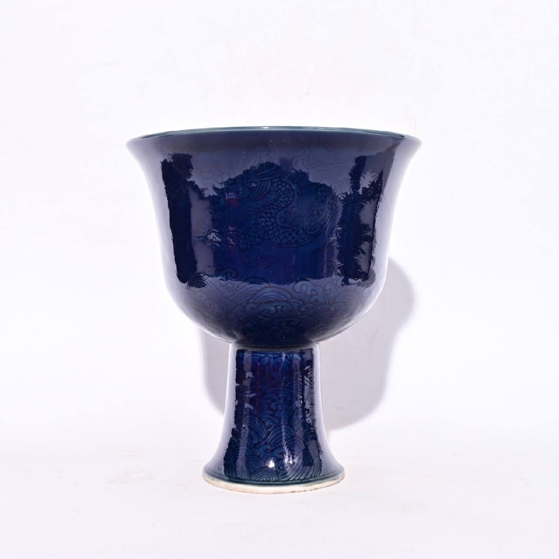 A high-footed cup with a carved dragon design: A high-footed cup with a carved dragon design in blue glaze, made during the Xuande reign of the Ming Dynasty, measuring 21 x 18.5 cm in height.