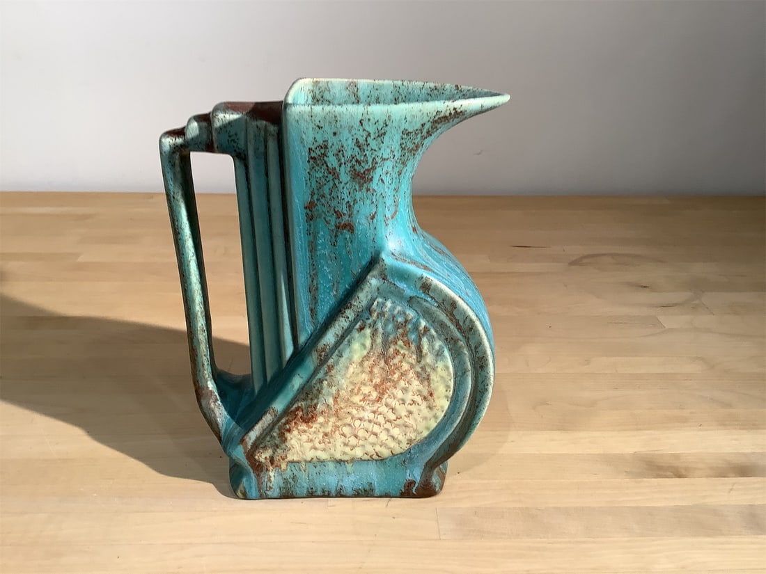 Belgian Art Deco Pottery Pitcher: Belgian Art Deco pottery pitcher features a unique design characterized by its elegant curves and geometric shapes. The vibrant turquoise glaze harmonizes beautifully with accents of earthy tones,