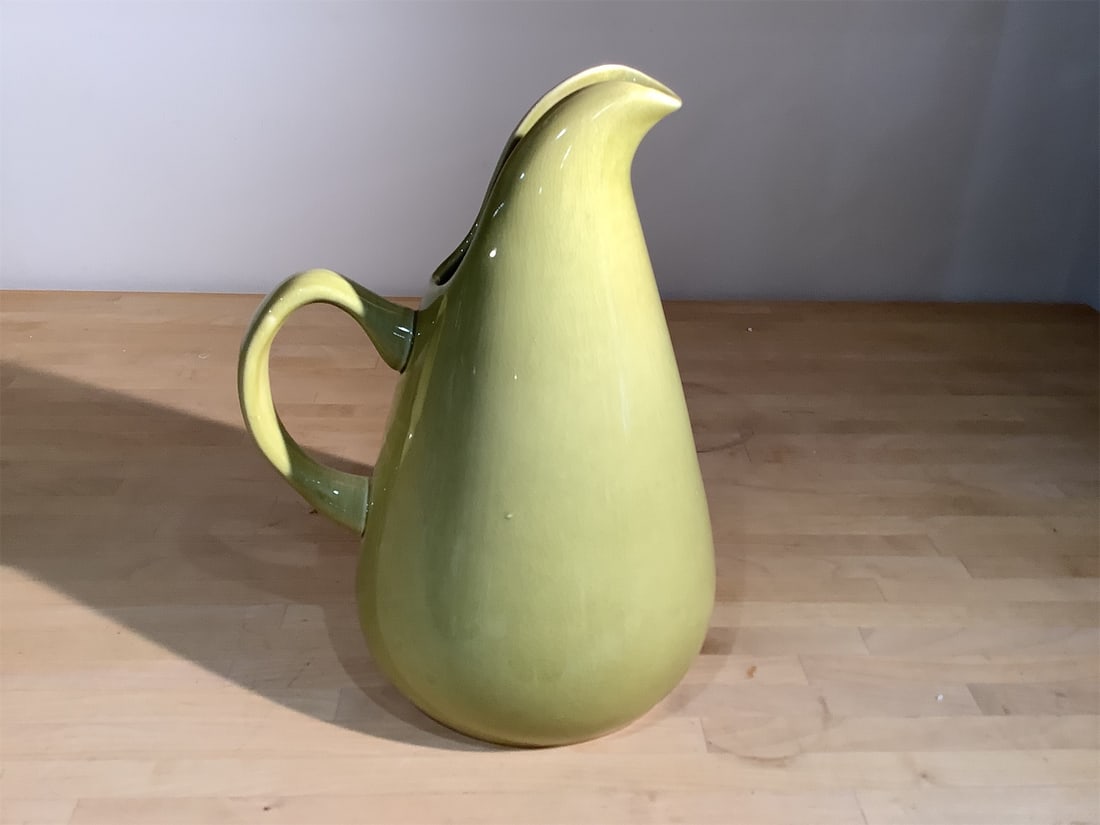 Russel Wright American Modern Pitcher: Russel Wright "American Modern" pitcher showcases a sleek, modern design with graceful curves and a vibrant yellow-green glaze. Its generous size and artful shape make it an eye-catching centerpiece